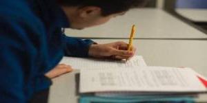 穿着蓝色运动衫的学生在教室里用铅笔做笔记