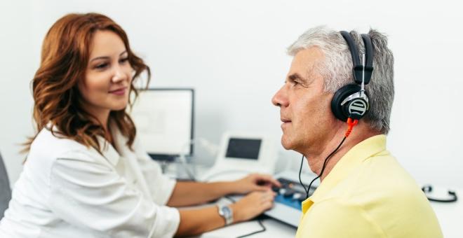 听力学医生与一位戴着耳机的病人一起工作.