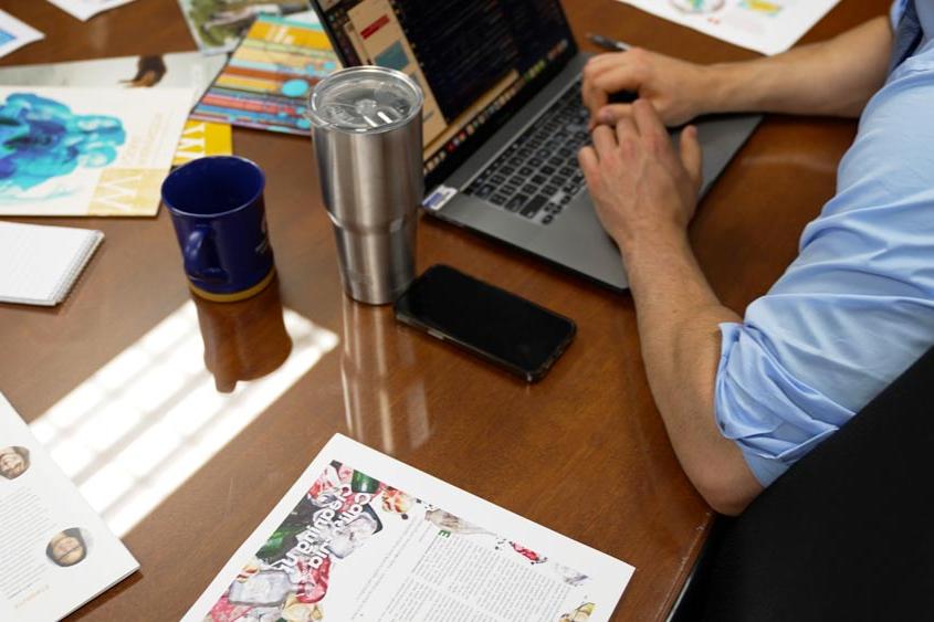 一个男人在电脑前打字，桌子上放着品牌宣传材料.