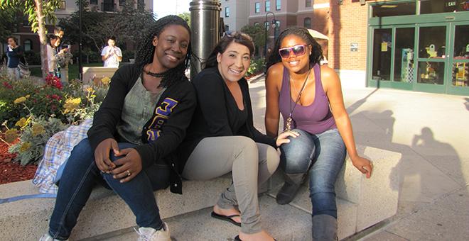 Three students sitting on a bench outside of a building on campus.
