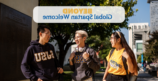 Beyond Global Spartan Welcome - three students wearing university garb talk with 一个 another