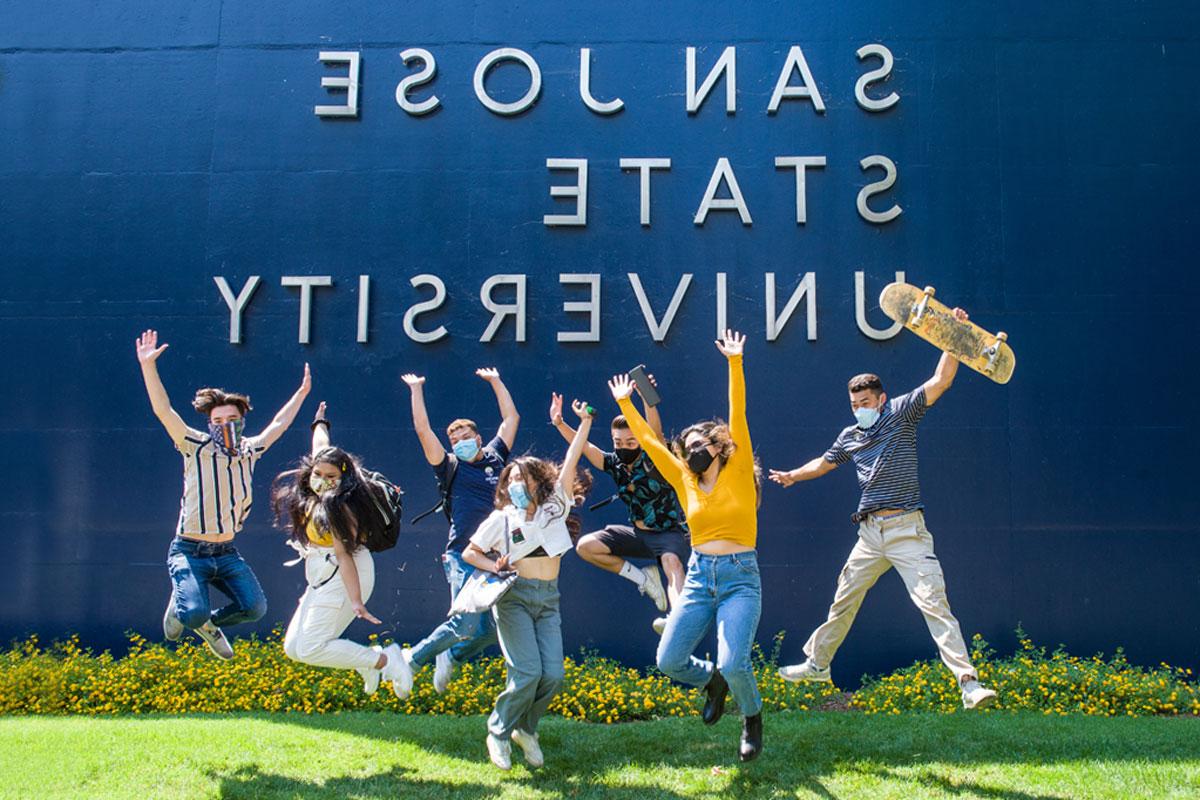 学生们在一堵写着圣何塞州立大学的墙前跳跃.